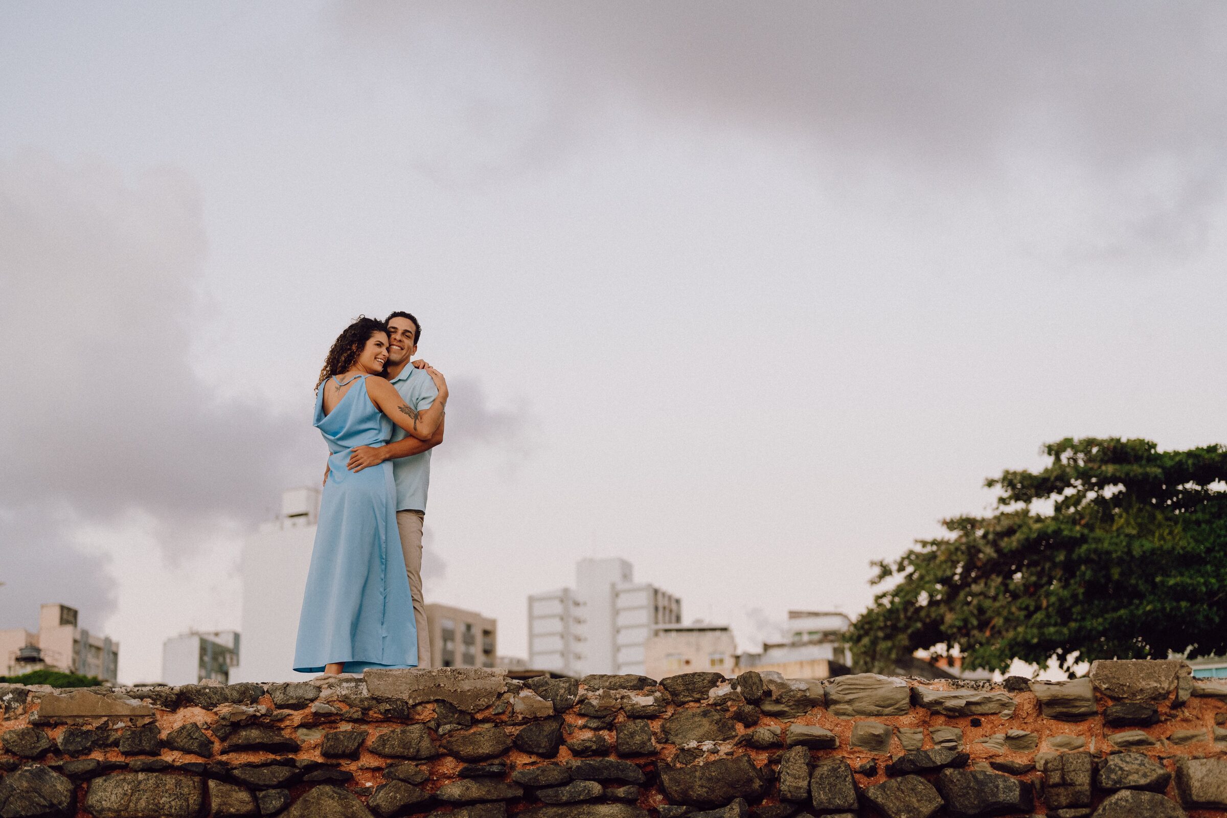 Leo e Tai abraçados sobre um muro, com o horizonte da cidade ao fundo