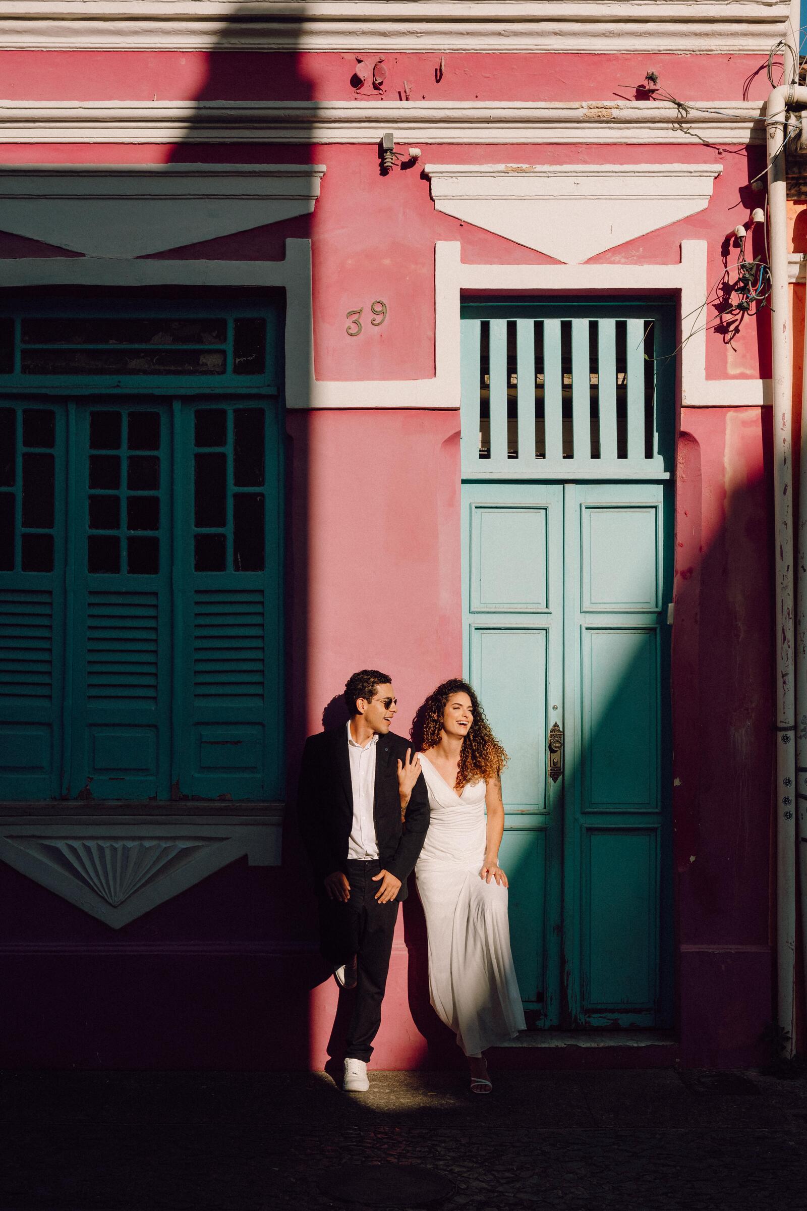 Leo e Tai em frente a um casarão rosa com portas azul-esverdeadas, no centro histórico de Salvador