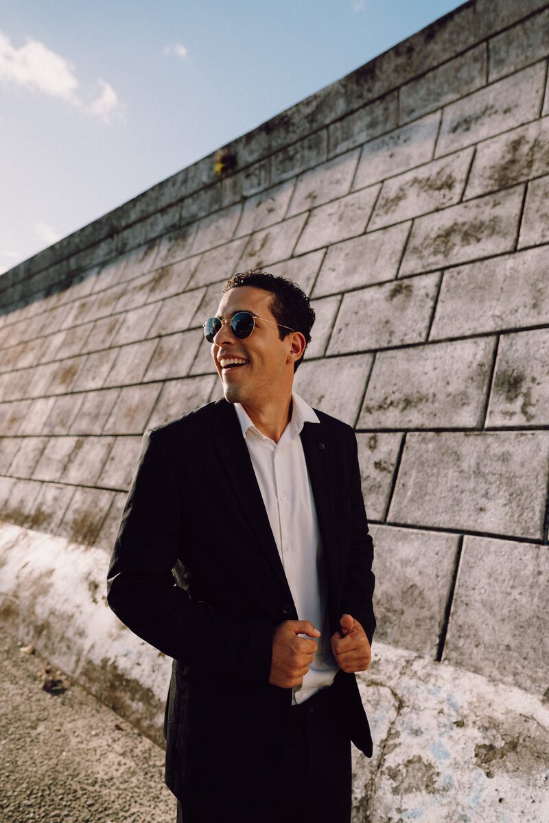 Leo de óculos escuros encostado em um muro de pedra