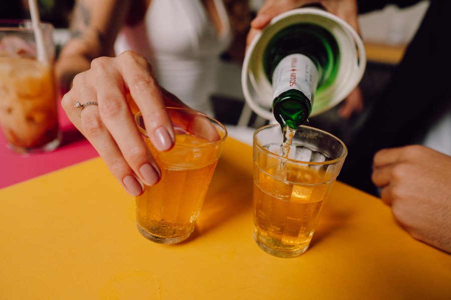 Mão servindo bebida em copos americanos sobre mesa de boteco