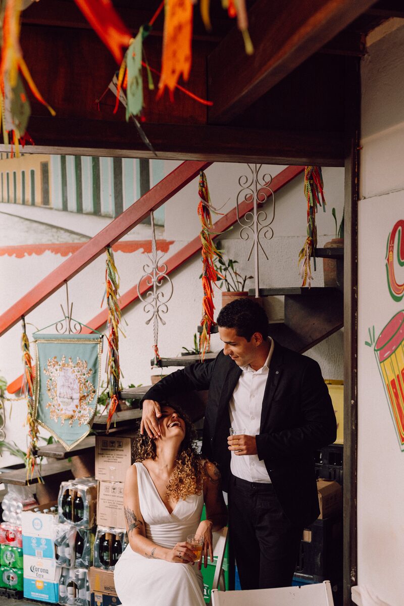 Leo e Tai rindo em um boteco decorado com bandeirolas coloridas