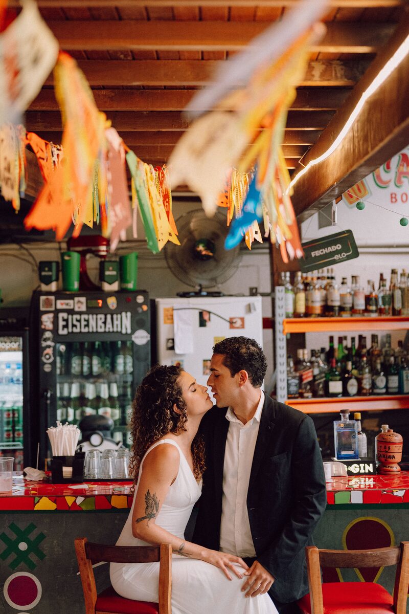 Leo e Tai próximos, sorrindo, em um bar de bairro histórico