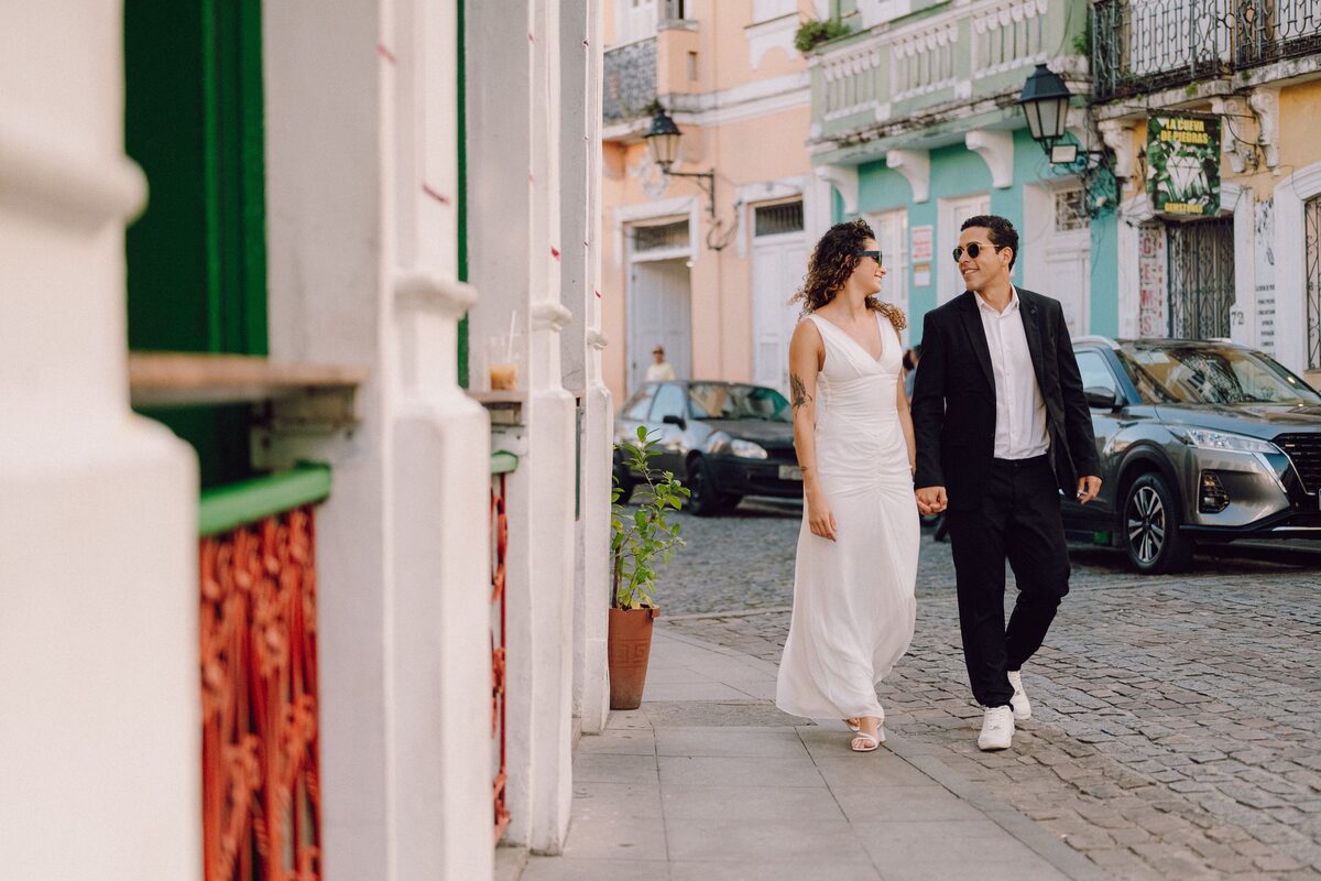 Leo e Tai andando de mãos dadas por uma rua colorida do centro histórico